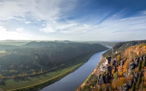 Foto der herbstlichen Szenerie eines Flusses, eines Waldes und einer Hügellandschaft.