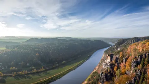 Foto der herbstlichen Szenerie eines Flusses, eines Waldes und einer Hügellandschaft.