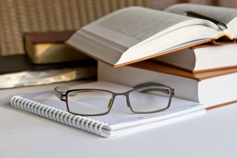 Fotostillleben mit einem geöffneten Buch, einem Notizbuch, auf dem eine Brille liegt
