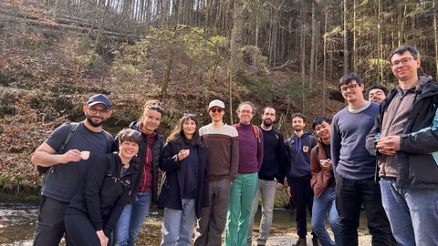 Mitglieder des Instituts in einem Wald, die aus weißen Tassen trinken und für ein Foto posieren.