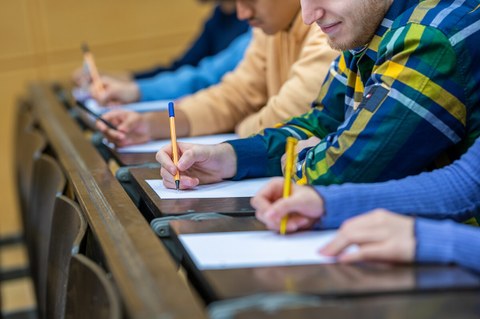 Bild zeigt fünf Studierende, die nebeneinander im Hörsaal sitzen und eine Prüfung schreiben.