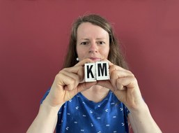 Kathleen vor rotem Grund mit Buchstaben in der Hand