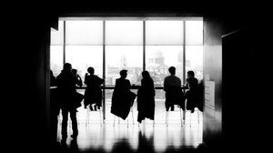 Das Foto zeigt die Silhouette mehrerer Personen, die sich an einem Tisch sitzend unterhalten in schwarz weiß.