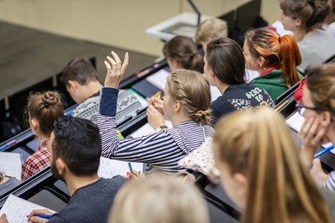 Foto von Studierenden in einer Vorlesung in einem Hörsaal. Eine davon meldet sich.