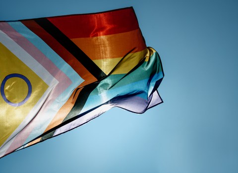 Die intersektionale Prideflag weht im Wind vor einem blauen Himmel.