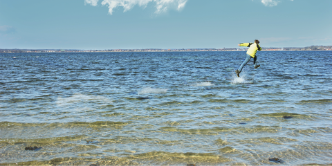 Ein Mensch rennt im flachen Wasser am Strand, sodass es aussieht als würde er über Wasser gehen.  