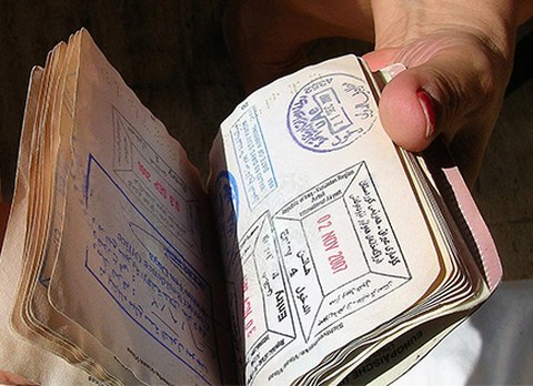 Zu sehen ist eine Hand, die einen Pass mit allerlei Visastempeln durchblättert. 