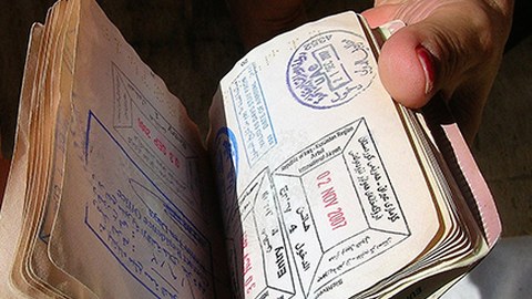 Zu sehen ist eine Hand, die einen Pass mit allerlei Visastempeln durchblättert. 