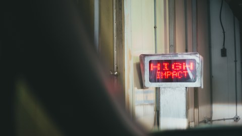 Ein alter Korridor in dem ein Monitor steht, auf dem in rot leuchtender, Pixelschrift "High Impact" zu lesen ist.