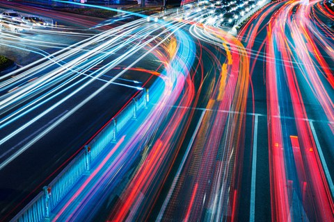 Foto: Bunte Verkehrslichter auf einer großen vielbefahrenen Straßenkreuzung in Zeitraffer bei Nacht.