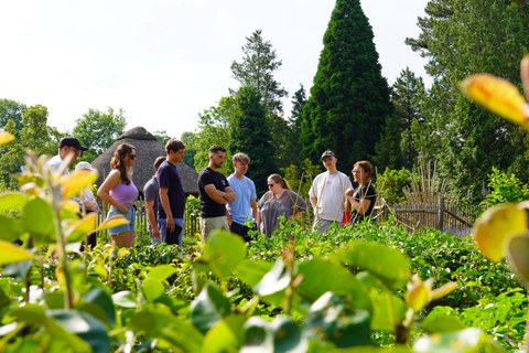 Ackercoachin und Dozentin Heidelinde Wutzler und eine Gruppe Student:innen in einem Garten. Im Vordergrund Pflanzen. 