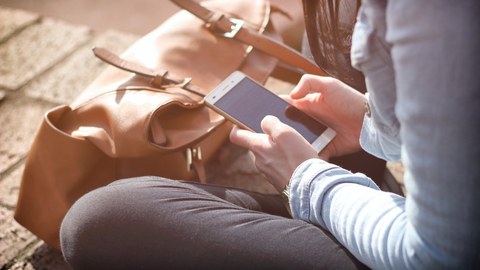 Eine Frau schaut im Sitzen auf ihr Mobiltelefon. 