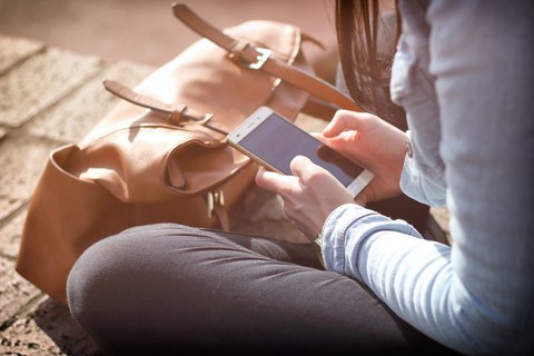 Eine Frau schaut im Sitzen auf ihr Mobiltelefon. 