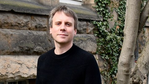 Portraitbild von Dr. Manes Weisskircher im Freien vor einigen Bäumen.