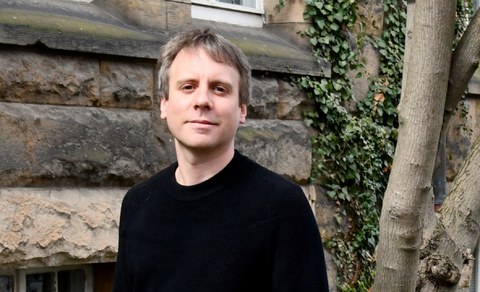 Portraitbild von Dr. Manes Weisskircher im Freien vor einigen Bäumen.