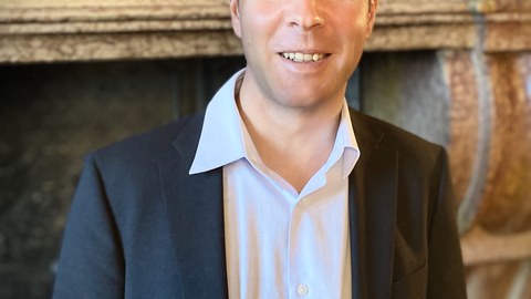 Porträtfoto von Stefan Feddern: Er lächelt frontal in die Kamera. Im Hintergrund ist ein historischer Steinkamin zu erahnen.