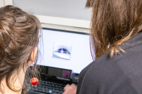 Zwei Frauen schauen auf einen Bildschirm, auf dem ein Auge mit Fadenkreuz zu sehen ist