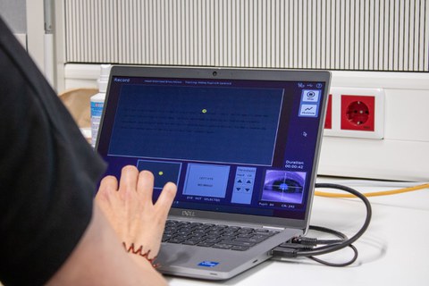 Eine Hand am Laptop, unten rechts ist das Auge der Probandin zu sehen