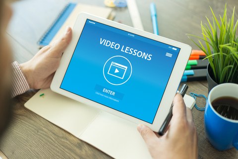 Mann am Arbeitsplatz, der auf ein Tablet blickt auf dem steht "Video Lessons", ein Play-Pfeil und "ENTER"