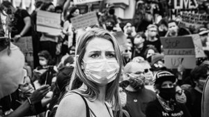 S/W-Bild einer jungen Demonstrationsteilnehmerin mit Maske