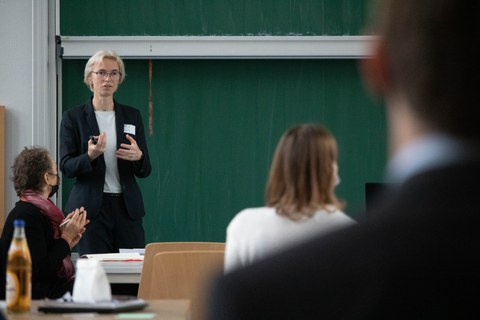 Prof. Regine Gerike steht vor einer Tafel und begrüßt die Teilnehmer:innen