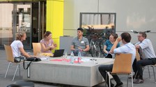 Gruppenarbeit: Teilnehmende sitzen im Freien vor einem Gebäude um ein Stadtmöbel