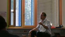 Prof. Christian Prunitsch sitzt auf einem Tisch und gestikuliert