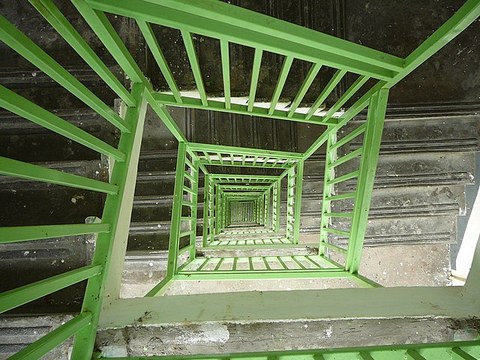 Zu sehen ist ein spiral abwärts laufendes grünes Treppengeländer.