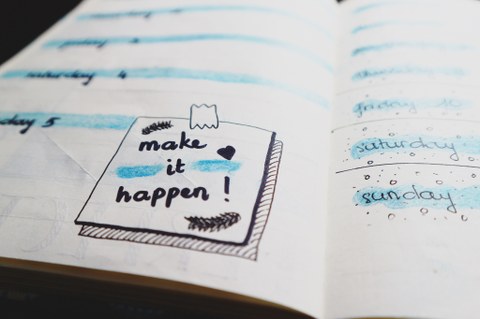 Es ist ein Schriftzug auf einem Taschenkalender zu sehen: "Make it happen" 