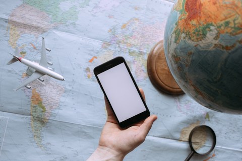 Zu sehen ist eine Landkarte, auf der ein Globus steht. Eine Hand mit einem mobilen Endgerät wird über die Karte gehalten. 