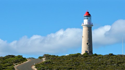 Zu sehen ist, ein weißer Leuchtturm mit rotem Dach auf einem Hügel.