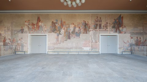 Foto eines Wandgemäldes: Das Gemälde zeigt über die gesamte Wand den Dresden-Besuch des Staatspräsidenten der DDR, Wilhelm Pieck. Er ist umringt von Menschen verschiedenen Alters, teils mit Fahnen, Werkzeugen, Büchern, Blumensträußen.