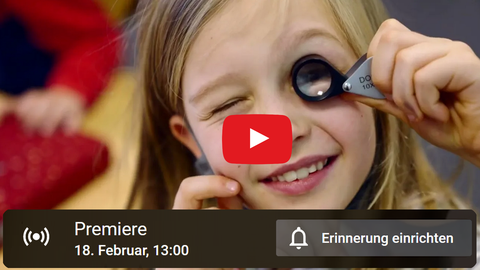 Bildcollage: Eine Schülerin der Universitätsschule Dresden hält eine kleine Lupe vors Auge und schaut direkt in die Kamera. Darüber liegt das YouTube-Logo, ein weißer Pfeil in rotem Rechteck. Text: Premiere 18. Februar 13 Uhr.
