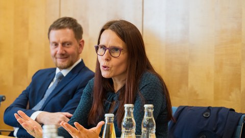 Prof. Langner und Ministerpräsident Kretschmer sitzen nebeneinander an einem Besprechungstisch bei der Auftaktveranstaltung zu "Schule bewegt Sachsen" in der Sächsischen Staatskanzlei. Anke Langner spricht, Michael Kretschmer schaut sie von der Seite an und lächelt zustimmend.