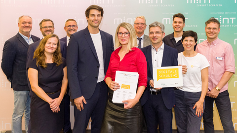 Elf Personen stehen mit Urkunde und Signet "Digitale Schule" vor einer MINT-Fotowand. In der Mitte Digitalbeauftragter Timo Wulff und Schulleiterin Maxi Heß von der Universitätsschule Dresden..