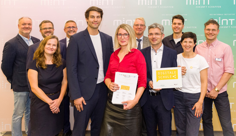 Elf Personen stehen mit Urkunde und Signet "Digitale Schule" vor einer MINT-Fotowand. In der Mitte Digitalbeauftragter Timo Wulff und Schulleiterin Maxi Heß von der Universitätsschule Dresden..