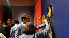Vor einer dunkelblauen Ausstellungswand stehen Direktor Prof. Dr. Holger Jacob-Friesen und eine Frau. Sie nehmen eines der abnehmbaren Bilder in die Hand.