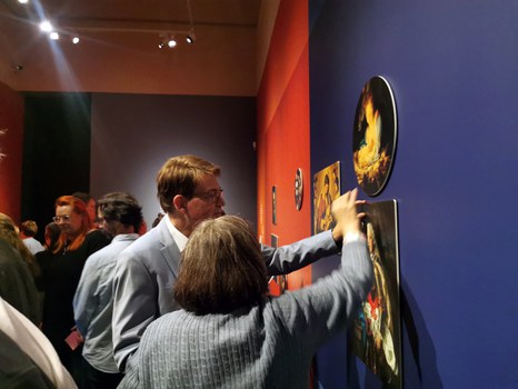 Vor einer dunkelblauen Ausstellungswand stehen Direktor Prof. Dr. Holger Jacob-Friesen und eine Frau. Sie nehmen eines der abnehmbaren Bilder in die Hand.