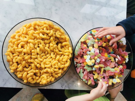 Zwei große Schüsseln mit bunten Gummibärchen und Erdnussflips. Zwei Kinderhände greifen nach Gummibärchen.