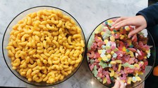 Zwei große Schüsseln mit bunten Gummibärchen und Erdnussflips. Zwei Kinderhände greifen nach Gummibärchen.