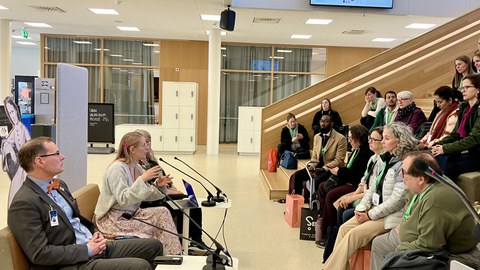 In einer Diskussionsrunde sitzen drei Personen sitzen mit Mikrofon vor einem Konferenzpublikum.