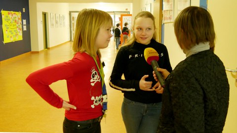 Zwei Schülerinnen stehen im Flur der Universitätsschule Dresden. Sie sprechen in das Mikrofon der Reporterin.
