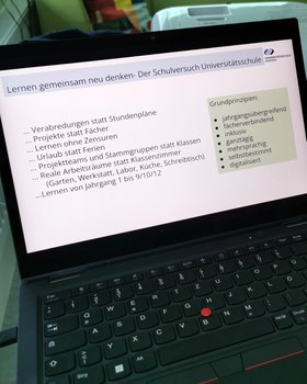 Blick auf ein Laptop mit der Präsentation „‎Lernen gemeinsam neu denken- Der Schulversuch Universitätsschule Dresden: Verabredungen statt Stundenpläne, Projekte statt Fächer, Lernen ohne Zensuren, Urlaub statt Ferien, Projektteams und Stammgruppen statt Klassen, Reale Arbeitsräume statt Klassenzimmer (Garten, Werkstatt, Labor, Küche, Schreibtisch), Lernen von Jahrgang 1 bis 9/10/12; Grundprinzipien: jahrgangsübergreifend, fächerverbindend, inklusiv, ganztägig mehrsprachig, selbstbestimmt, digitalisiert."
