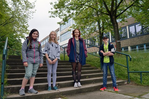 3 Schülerinnen und eine Studentin stehen auf der Treppe vor dem Schulgebäude