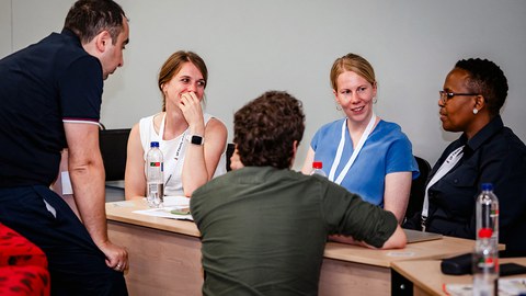 Fünf Personen sitzen um einen Konferenztisch und diskutieren.