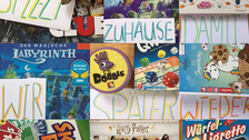 Blick von oben auf 3x3 Verpackungen von Gesellschaftsspielen, zum Beispiel ein Harry-Potter-Spiel. Auf und zwischen den Boxen liegen Zettel mit einzenen Wörtern. Die Wörter ergeben den Satz "Spielt zuhause, damit wir später wieder zusammen spielen können."