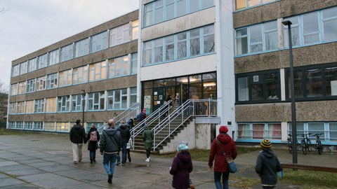 Viele Personen betreten über eine Treppe in den DDR-Schulbau der Universitätsschule Dresden.