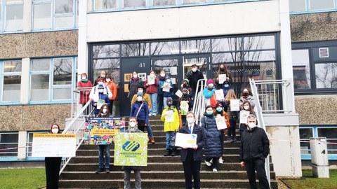 Auf der Treppe vor dem Schulgebäude steht die Delegation mit dem Spendenscheck, Million-Pixel-Bild und der Mappe mit den Unterschriften