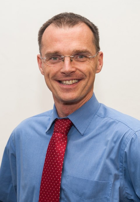 Portrait von Prof. Dr. Rolf Koerber, Mitglied des Projekts Universitätsschule Dresden. Ein Mann mit kurzen dukelblonden Haaren, blauem Hemd, roter Krawatte und randloser Brille lächelt in die Kamera.