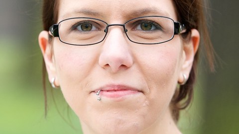 Potraitfoto von Gesine Wegner. Weiße Frau in den Zwanzigern mit Brille vor grünem, leich verschwommenen Hintergrund.